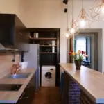 Modern communal kitchen area with a sink, dishwasher, washing machine, and cooking amenities for hostel guests.